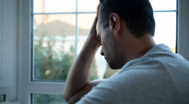 istock Depressed, sad, frustrated, crying, scared, instability mental and bipolar young man sitting on the windowsill at home. Headache because overworked and stress 2164855819