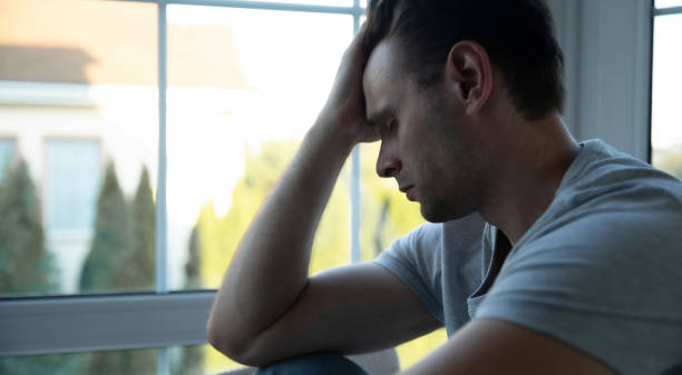 istock Depressed, sad, frustrated, crying, scared, instability mental and bipolar young man sitting on the windowsill at home. Headache because overworked and stress 2164855912