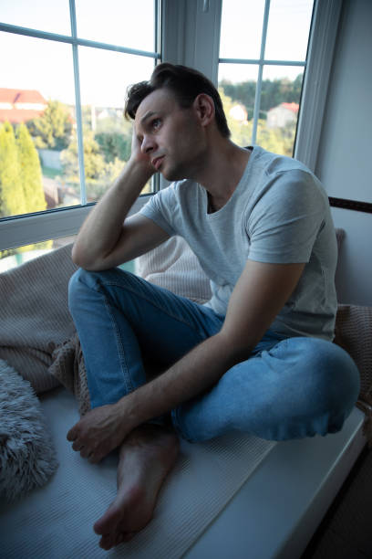 istock Depressed, sad, frustrated, crying, scared, instability mental and bipolar young man sitting on the windowsill at home. Headache because overworked and stress 2164856013