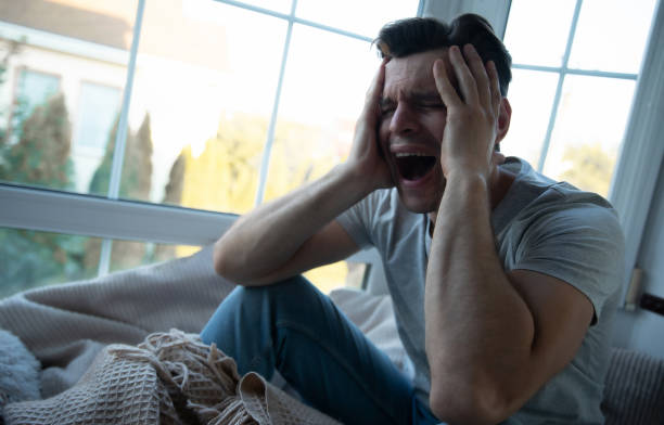 istock Depressed, sad, frustrated, crying, scared, instability mental and bipolar young man sitting on the windowsill at home. Headache because overworked and stress 2164856070
