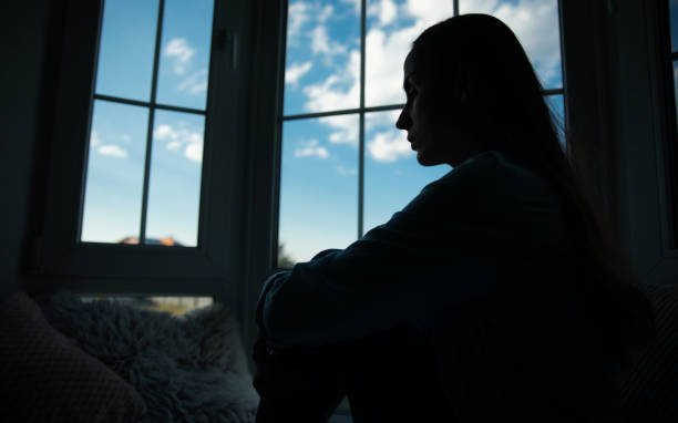 istock Close up side view of shadowed silhouette depressed woman while she sitting on windowsill with wide window on background. Sad, crisis, bad emotions, mental health, family violence. 2164856101