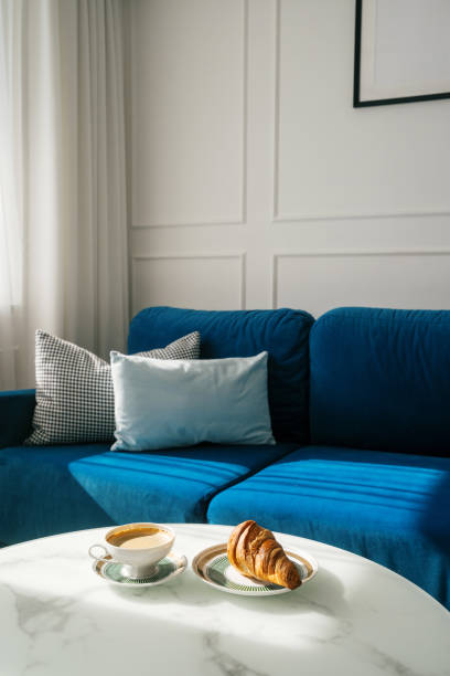istock Coffee and croissant on a side table in a living room with blue couch 2164864113