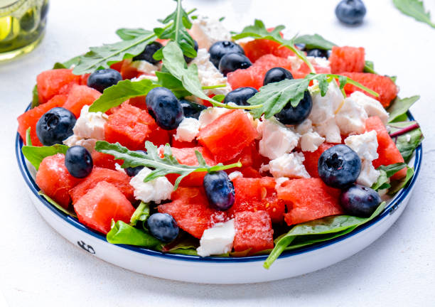 istock Summer fruit salad with watermelon,  cheese, blueberries and arugula on white background, top view 2164866324