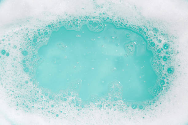Close-up of soap suds with round clean area on a turquoise blue background.
