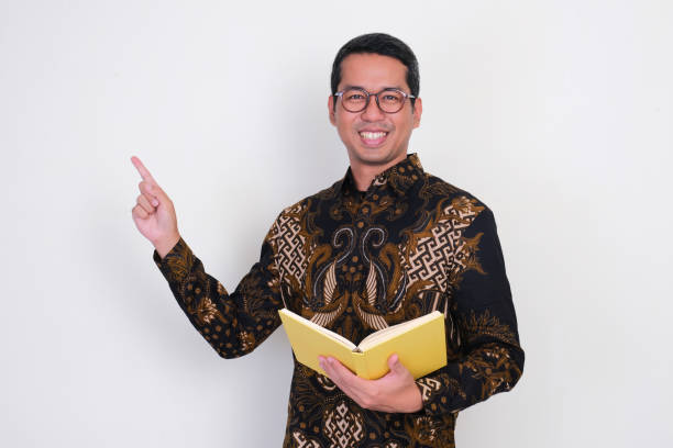 istock Adult Asian man smiling and pointing beside him while holding a book 2164874322