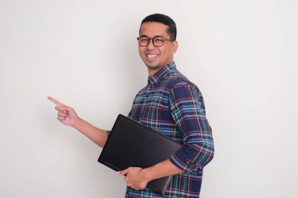istock Side view of a man smiliing and pointing beside him while holding a laptop 2164886696
