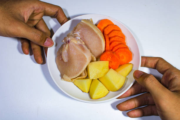 broiler chicken, cut potatoes and carrots, served on a white plate with two hands from above
