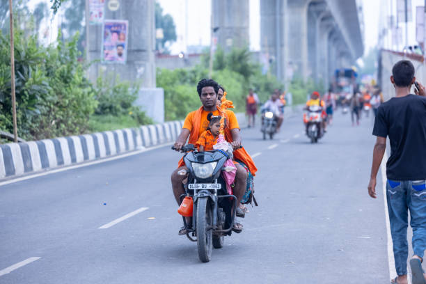 Ghaziabad, Uttar Pradesh, India - July 2024:  Group of hindu pilgrims performing kanwar yatra on two wheeler during sawan shivratri and carrying holy ganga water to worship god shiv with rituals.