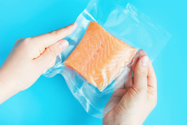 istock Female hands holding fish in vacuum packaging on blue background top view. 2164896457