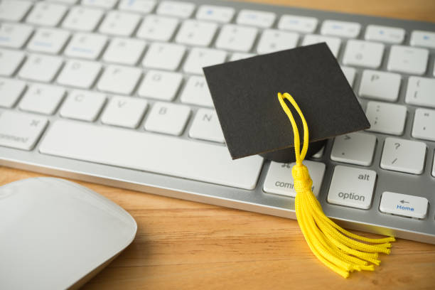 istock Graduation cap or mortarboard on keyboard computer wooden table background and mouse. 2164897470