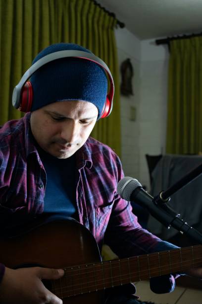 istock latino man with red headphones and wool cap practicing the guitar 2164905235