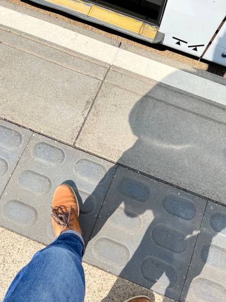 Customer with foot on tactile paving for visually impaired at edge of tram stop