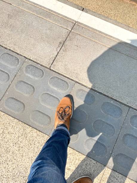 Customer with foot on tactile paving for visually impaired at edge of tram stop