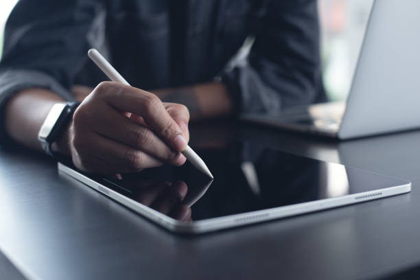 istock Business man, graphic designer using stylus pen on digital tablet screen while working on laptop computer on office table. Man in casual ware online working, surfing the internet on tablet pc 2164908184