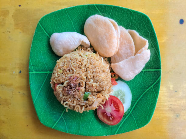 Nasi Goreng Magelangan Or Magelangan Fried Rice Is A Traditional Food From Magelang, Indonesia. Serving With Noodle, Tomato, Cucumber, Chopped Chives, Fried Onion, Sausage, Cracker Or Krupuk. Food Menu. Top View. nasi goreng magelangan o arroz frito de magelangan es una comida tradicional de magelang, indonesia. servir con fideos, tomate, pepino, cebollino picado, cebolla frita, salchicha, galletas saladas o kerupuk. menú de comida. vista superior.