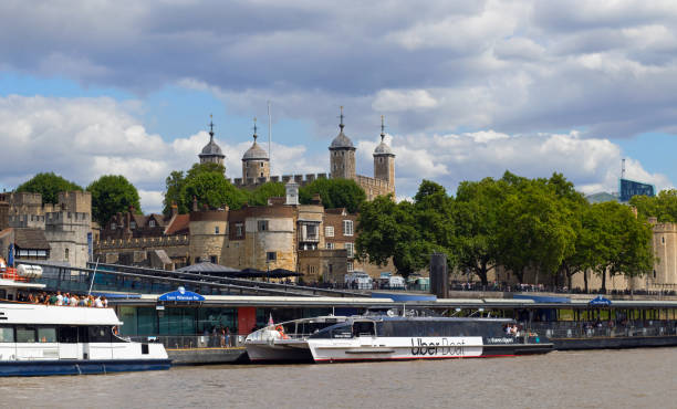 London, UK, 25-07-24. Tower of London with UBER transport boat in the foreground. The tower is a popular visitor attraction and UBER is a quick and efficient way to travel up the Thames. It is very busy with tourists in the Summer months