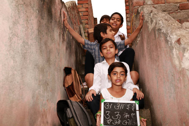 Cheerful elementary age school students sitting in a row at home in staircase holding chalkboard in hands wearing school uniform portrait close up.