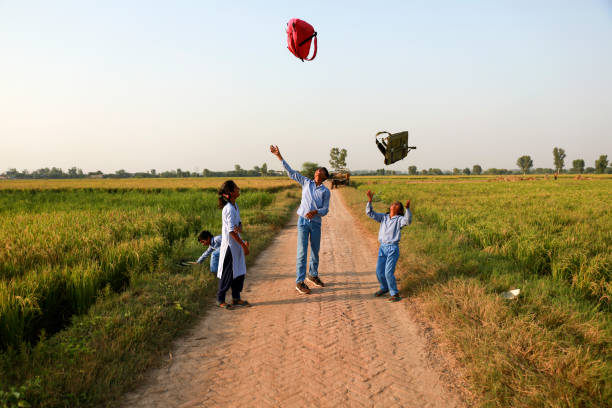 School students wearing school uniform throwing school bag in mid-air after vacation playful portrait outdoor in nature near green field during springtime.