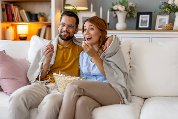 istock Couple laughing and eating popcorn on the couch. 2164934519