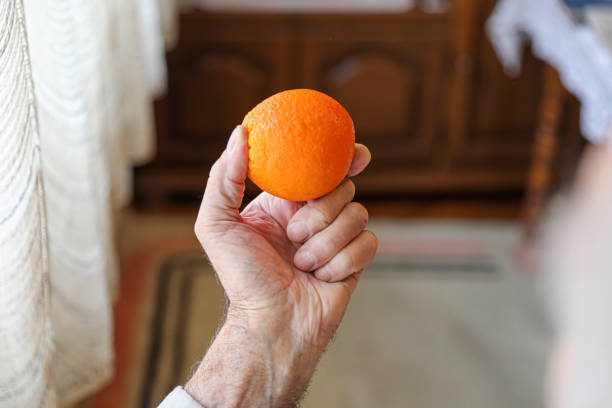 Detailed view of a senior man's hands as he carefully grasps an orange, showcasing the wrinkles and character of aging hands.