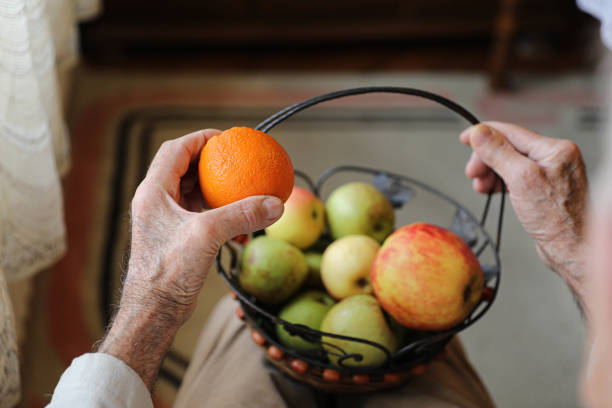 An intimate close-up of an elderly person’s hands as they select an apple from a basket filled with fresh fruits. This image highlights the daily routines and healthy lifestyle choices of seniors, focusing on fresh, nutritious food. Perfect for concepts related to senior care, healthy living, and nutrition.