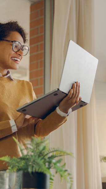 istock Female freelancer working laptop remotely while standing near window at home. Distance work concept 2164938739