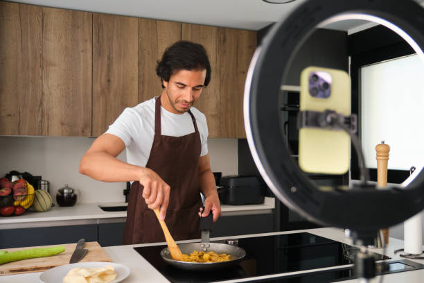 istock Young chef recording video with smartphone camera on tripod while cooking in kitchen 2164939003