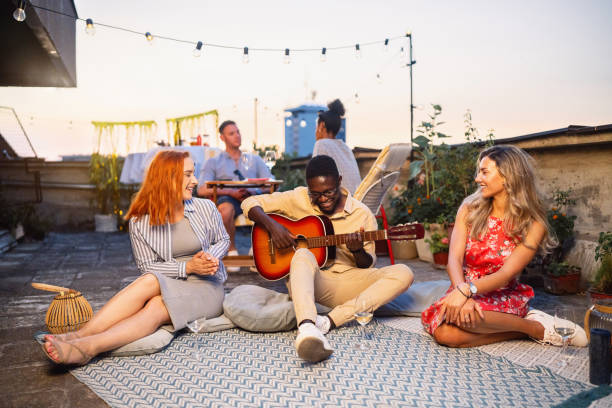 istock Man Black ethnicity playing acoustic guitar while hangout with friends on a rooftop during sunset 2164944564