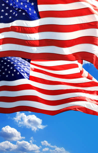 istock Waving American flags at flagpoles over sunny blue sky 2164951859