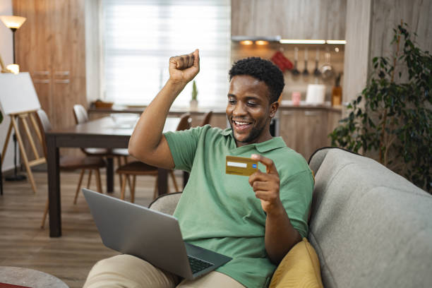 istock Excited black man on a sofa at home using laptop for online shopping 2164958004
