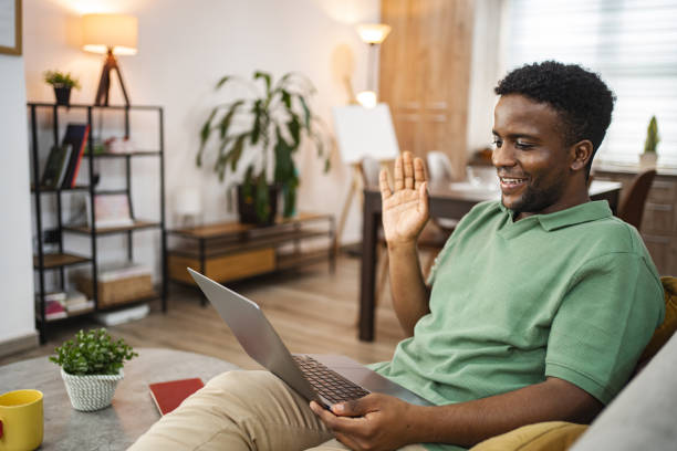 istock Young black man sitting on a sofa at home talking on a video call over laptop 2164958120