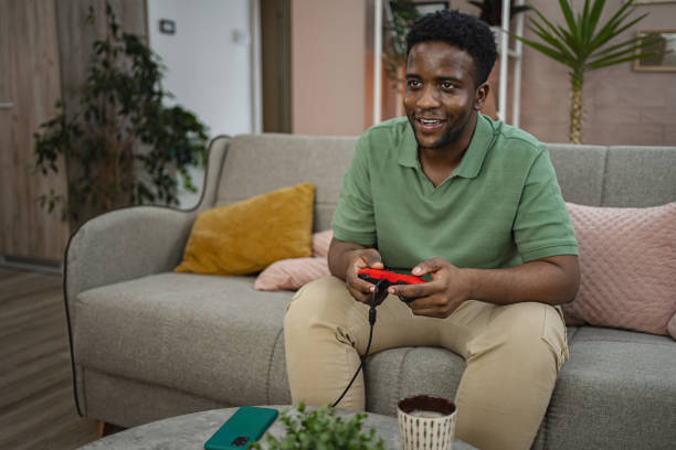 istock Young black man playing video games at home 2164958123