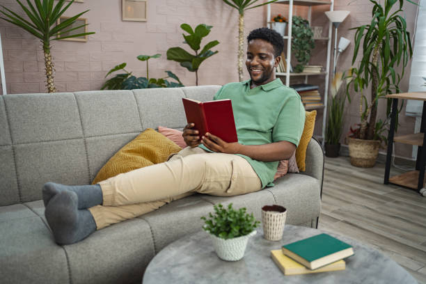 istock Young black man reading a book on a sofa at home 2164958193