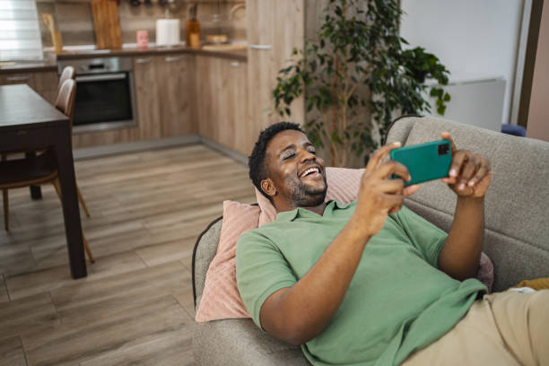 istock Young black man using mobile phone while relaxing on a sofa at home 2164958298