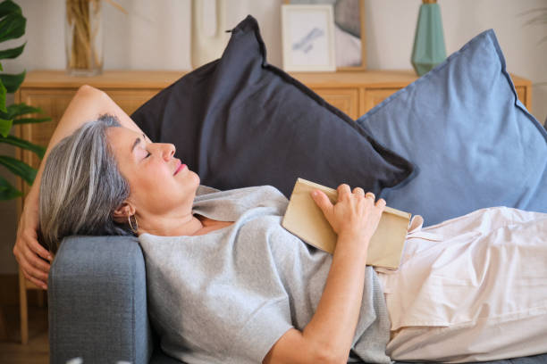 Senior woman falling asleep while reading a book on the sofa