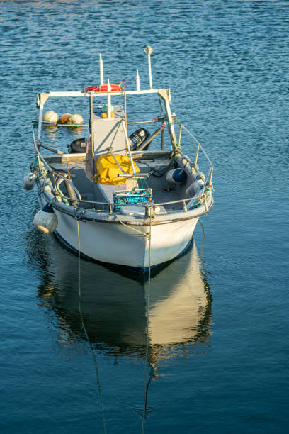 small fishing boat reflected in calm harbor waters in summer