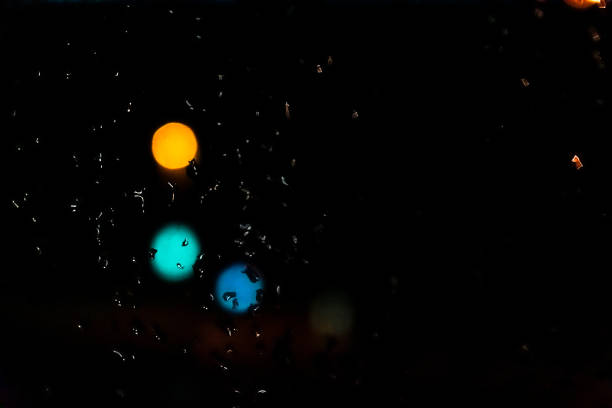 Mesmerizing urban bokeh through raindrops on window glass creating a cozy atmosphere. The glitter of bokeh city lights through the window.