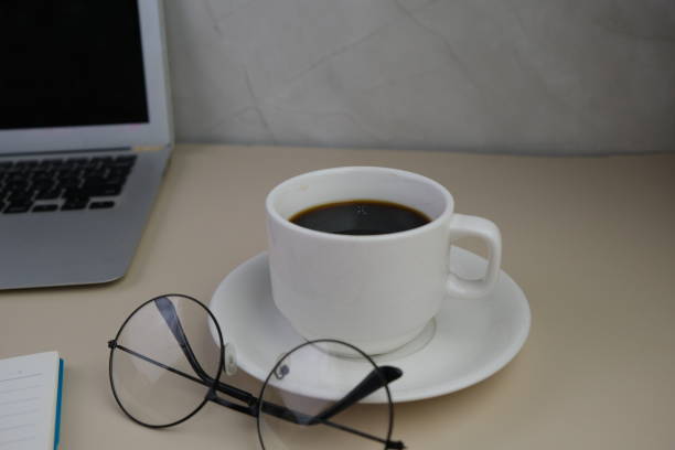 Coffee depression, empty coffee cup after drink with coffee stain of espresso on table with laptop, eyeglasses and spoon. Close up hot coffee Espresso in a white mug on red table background. Flat-lay, top view. Cup of coffee with pure black and brown. Copy space, food and drink concept.