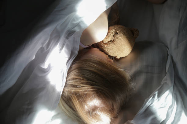 istock Child sleeping under white sheets hugging teddy bear. Children's nap time or bedtime. 2164976407