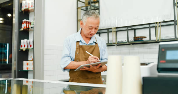 istock Senior Asian entrepreneurs man working using a digital tablet to manage orders in modern cafe. Small business owner. 2164979428
