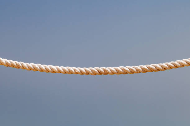 A close-up of a thick, coiled cotton rope resting on a light wooden surface. The image highlights the texture of the rope fibers against the smooth grain of the wood.