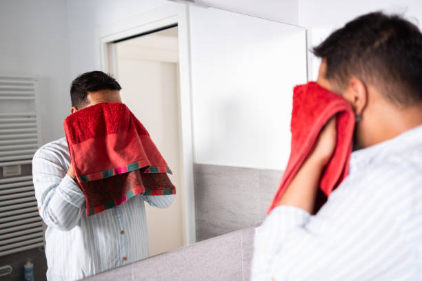 Man drying face with red towel in bathroom mirror