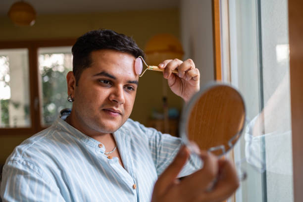 istock Man using jade roller for skincare in front of mirror at home 2164985914