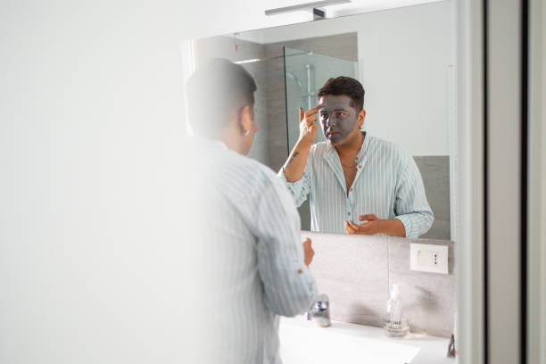 istock Man applying facial mask in bathroom mirror reflection 2164986001