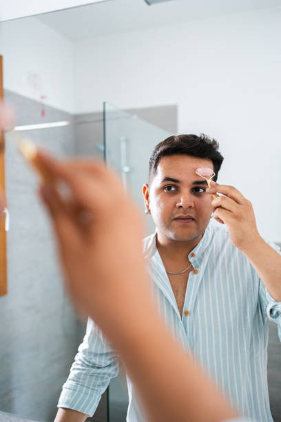 istock Man using facial roller for skincare in bathroom mirror 2164986045