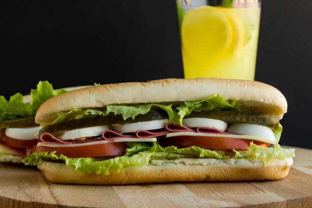 Close-up taken of Cold sandwich with egg, salami, tomato and pickle, with a glass of cold lemonade