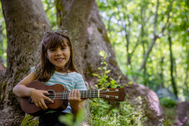 Portrait of smiling little girl looking at camera and playing ukulele.