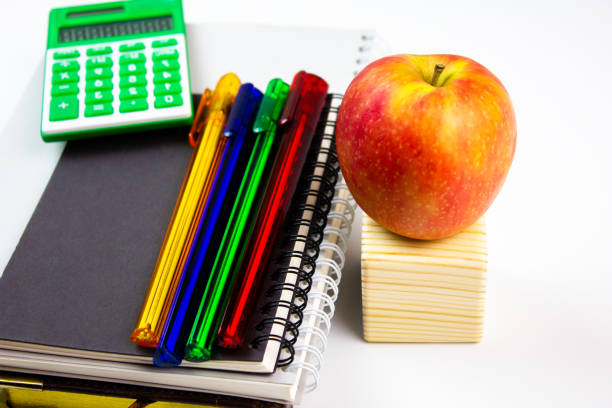 School supplies, on a white background. Pens on notebooks with calculator and apple.