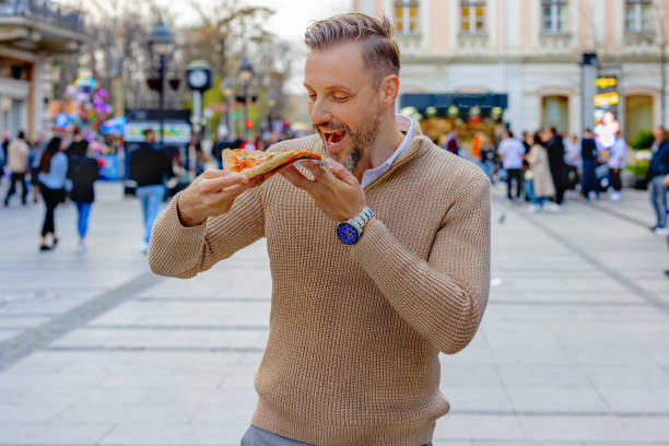 istock Young man enjoying pizza while walking through city streets 2165015804