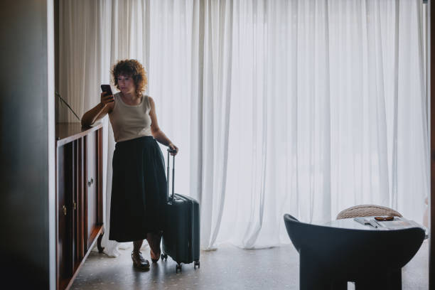 istock Woman Checking Mobile Phone in Hotel Lobby with Suitcase 2165024745